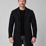 Homme portant un manteau noir à trois boutons, vu de face sur un fond gris uni.