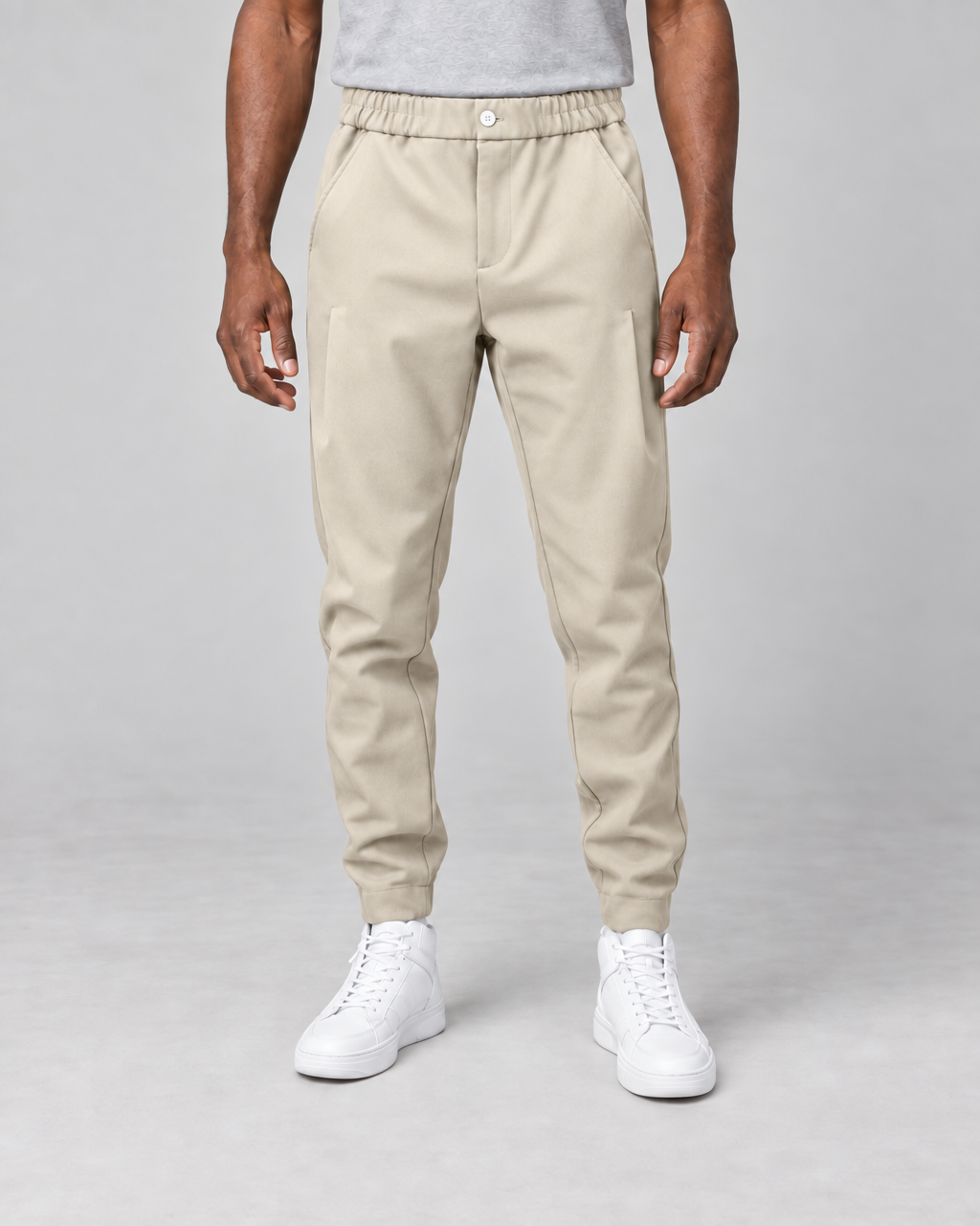Vue de face recadrée d’un pantalon beige à taille élastiquée, poches latérales et chevilles resserrées.