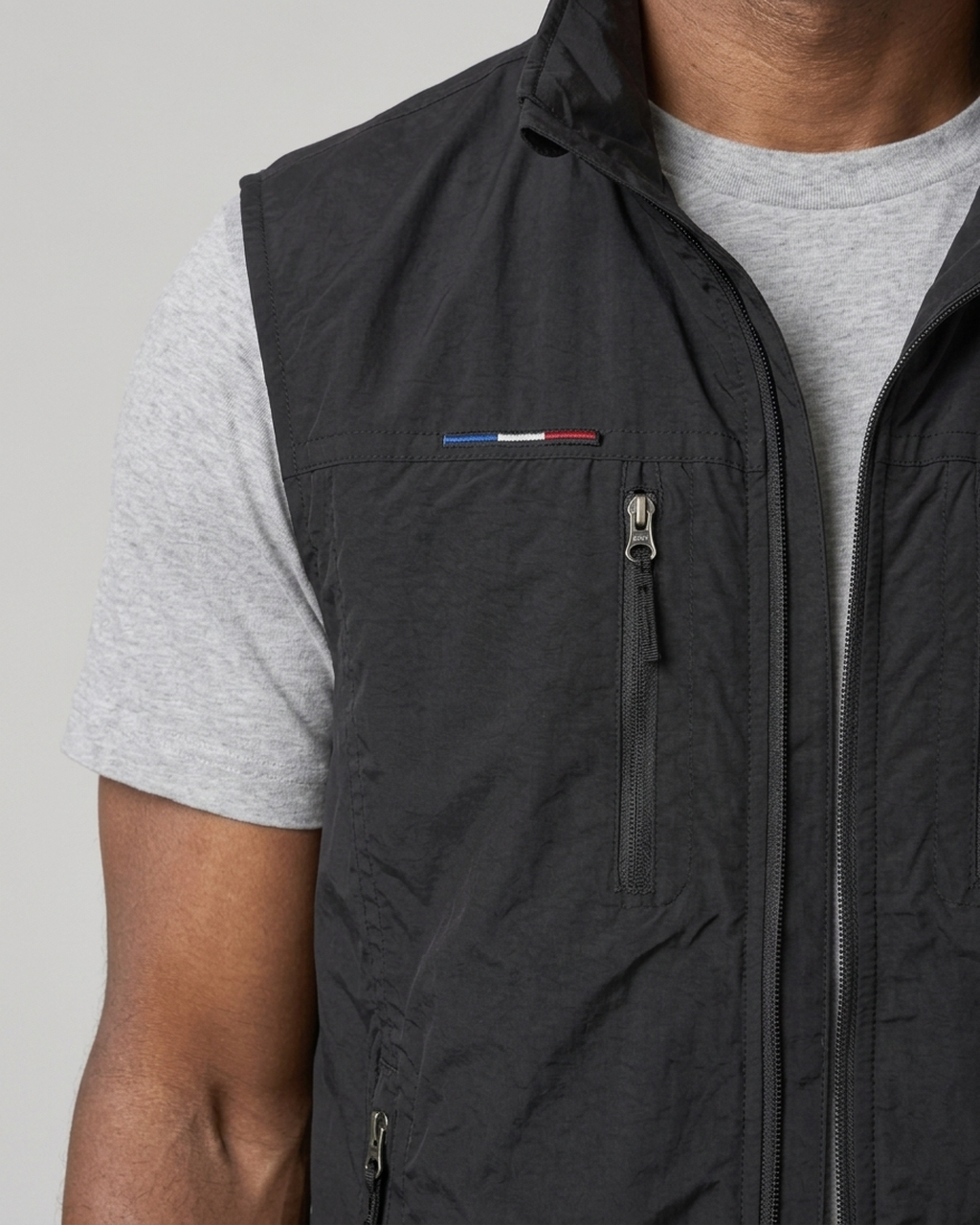 Gros plan de face d’un gilet sans manches noir zippé, avec poche poitrine verticale, porté sur un t-shirt gris