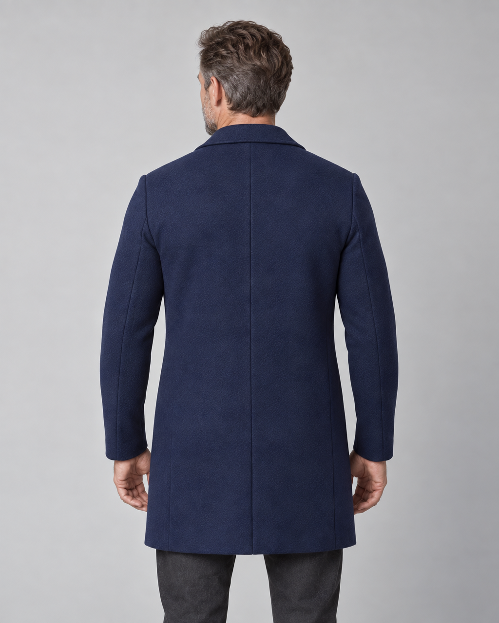 Vue arrière cadrée d’un manteau bleu marine mi-long porté par un homme.