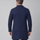 Vue arrière cadrée d’un manteau bleu marine mi-long porté par un homme.