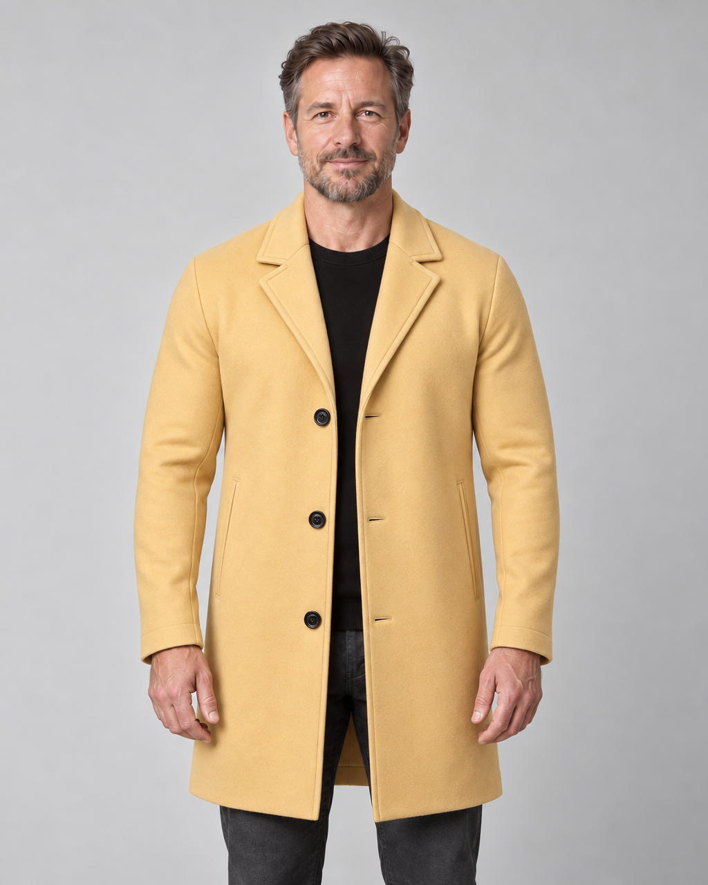 Vue de face recadrée d’un homme portant un manteau jaune moutarde à revers, trois boutons et poches latérales.