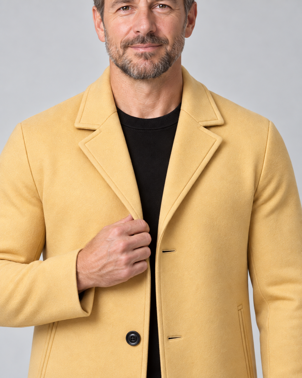Gros plan de face d’un homme portant un manteau jaune moutarde à revers et boutons noirs.