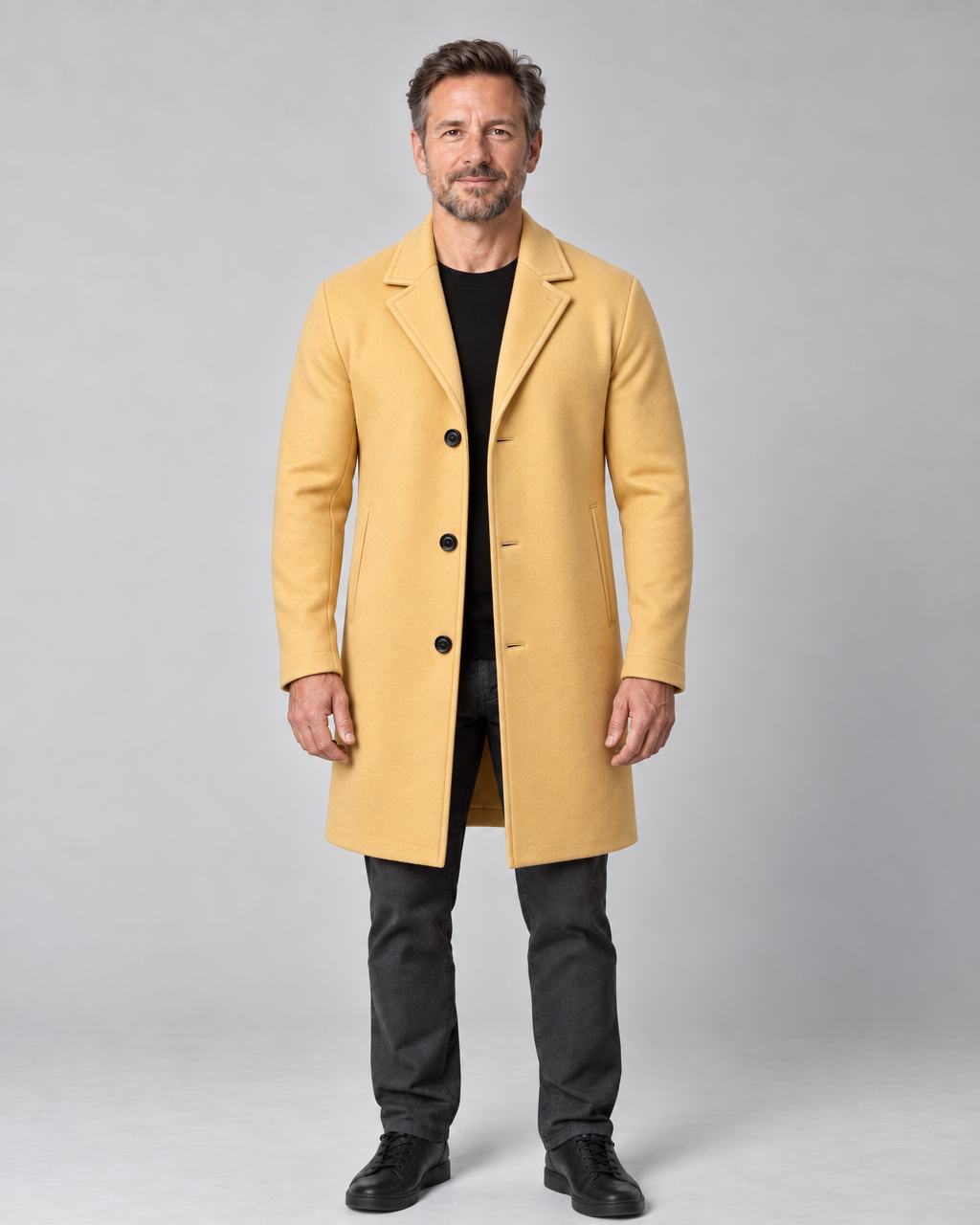 Homme en pied portant un manteau jaune ocre à trois boutons, vu de face.
