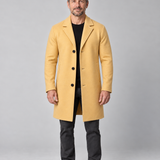 Homme en pied portant un manteau jaune ocre à trois boutons, vu de face.
