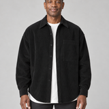 Veste-chemise noire à fines côtes, boutonnée, avec poche poitrine, vue de face cadrée à mi-cuisses.