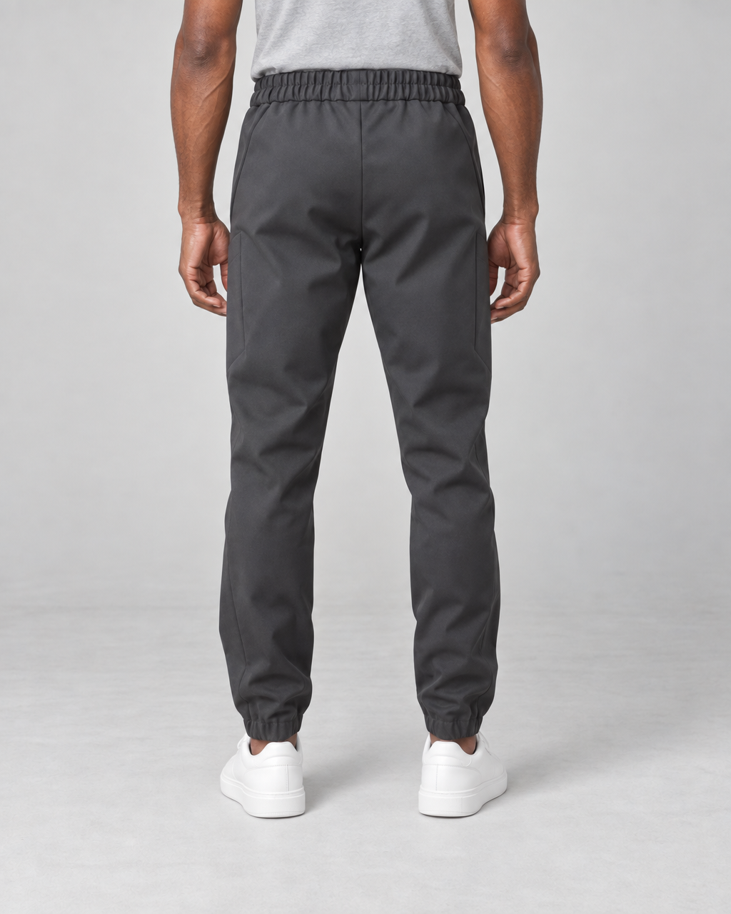 Vue arrière recadrée d’un pantalon gris foncé porté, avec taille et chevilles élastiquées.