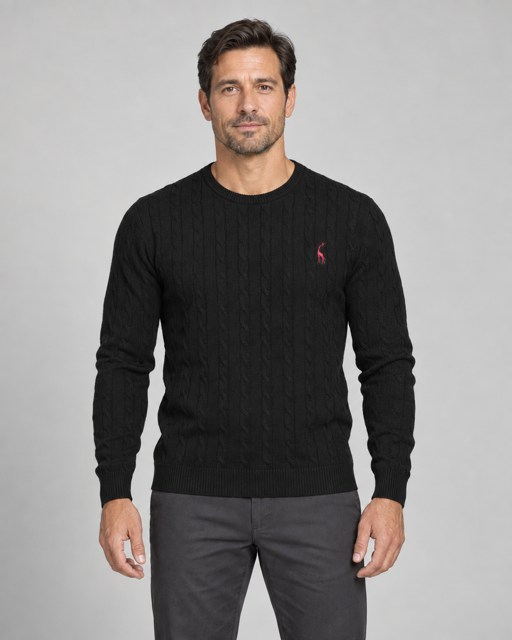 Vue de face cadrée d’un homme portant un pull noir torsadé à col rond avec petit motif rouge sur la poitrine.