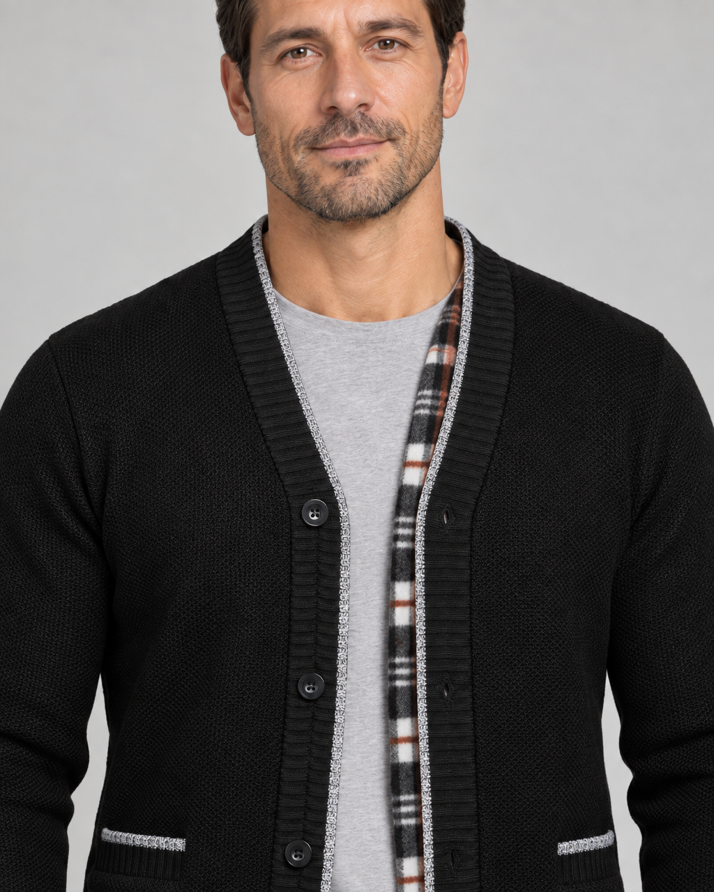 Vue rapprochée de face d’un cardigan noir à boutons, avec bordure grise et parement intérieur à carreaux.