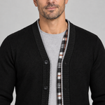 Vue rapprochée de face d’un cardigan noir à boutons, avec bordure grise et parement intérieur à carreaux.