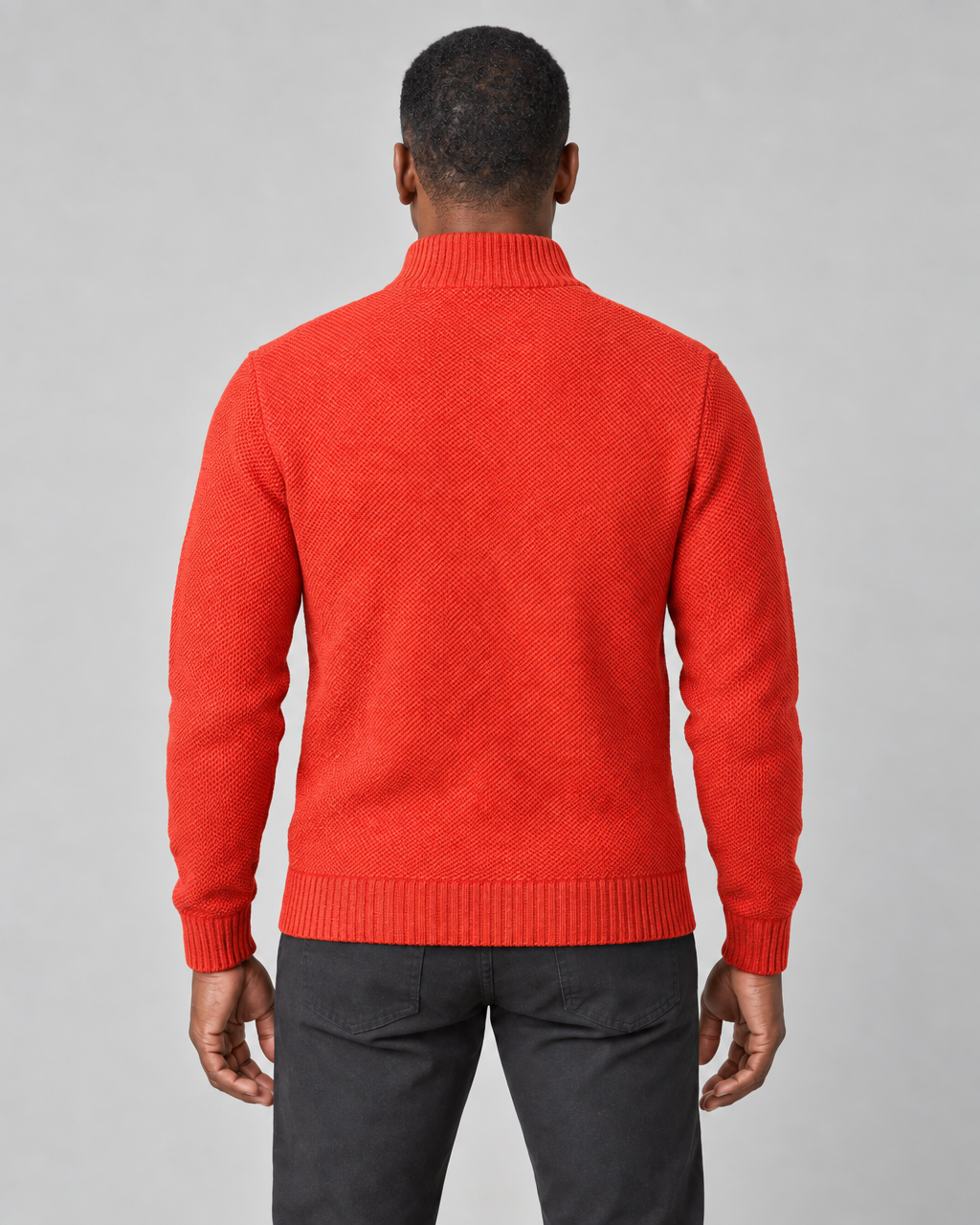 Vue de dos recadrée d’un homme portant un pull orange vif à col montant et manches longues.