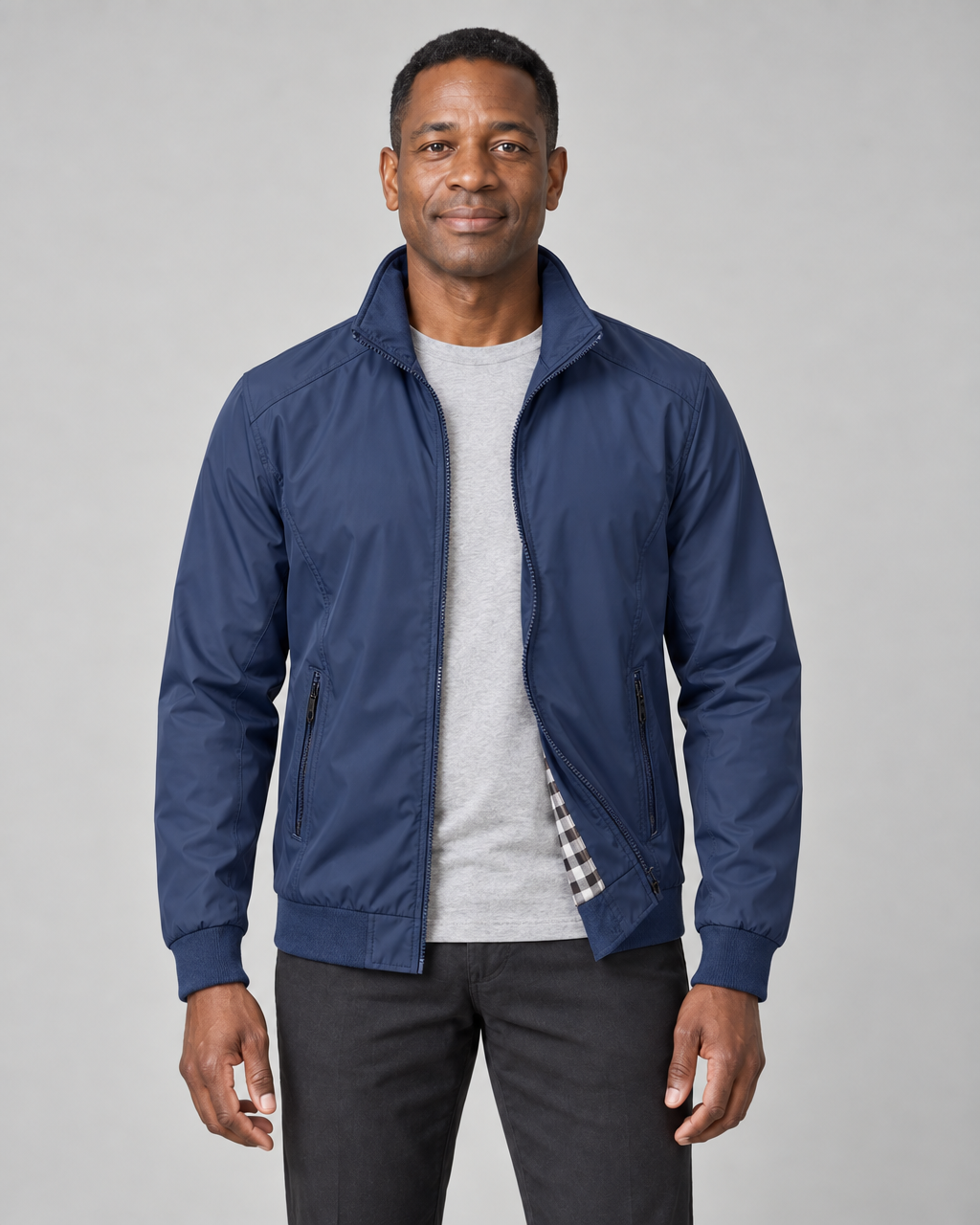 Homme de face portant une veste bleue zippée, ouverte, avec col montant et poches latérales zippées.