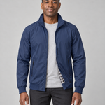 Homme de face portant une veste bleue zippée, ouverte, avec col montant et poches latérales zippées.