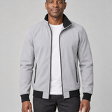 Homme de face portant une veste grise ouverte à col montant et poches zippées, vue cadrée de face.