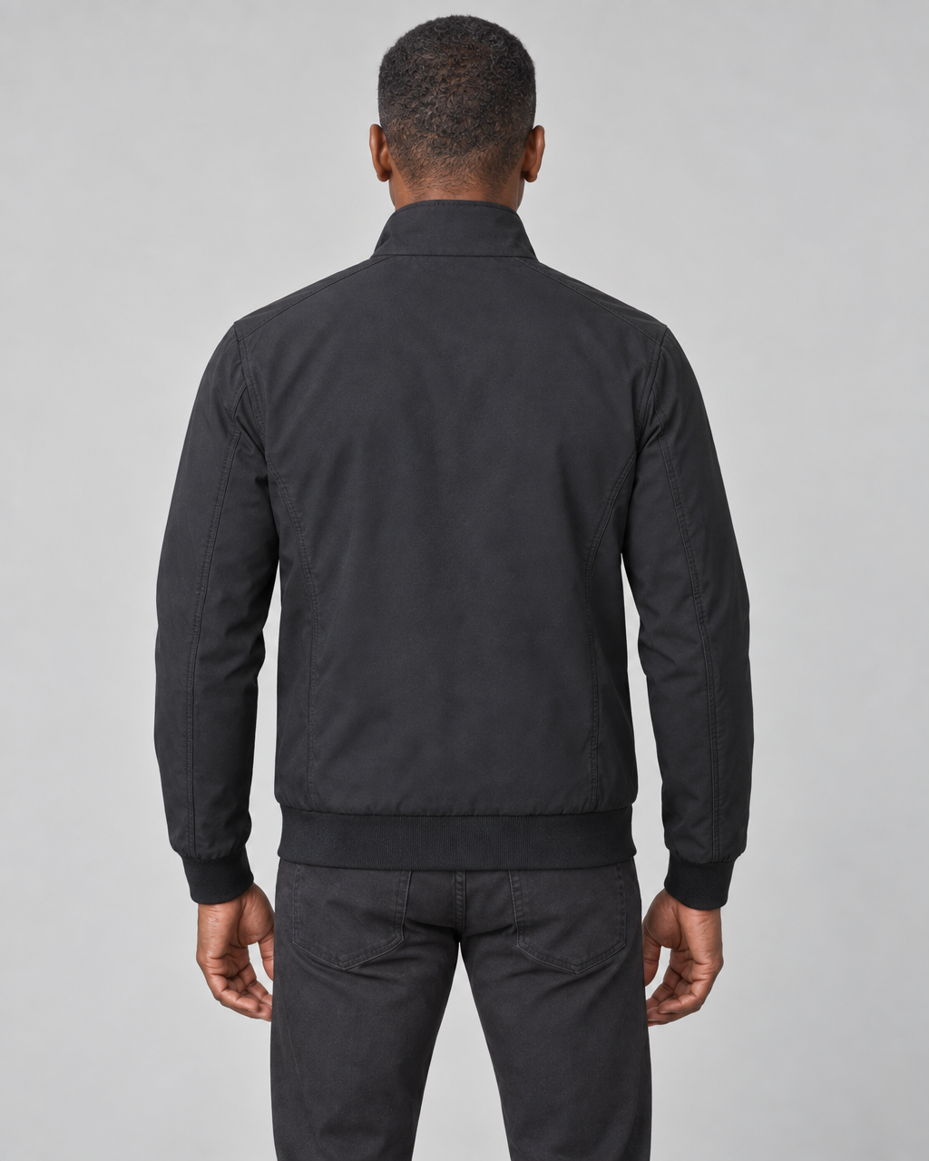 Homme de dos portant une veste noire à col montant, avec poignets et taille côtelés.